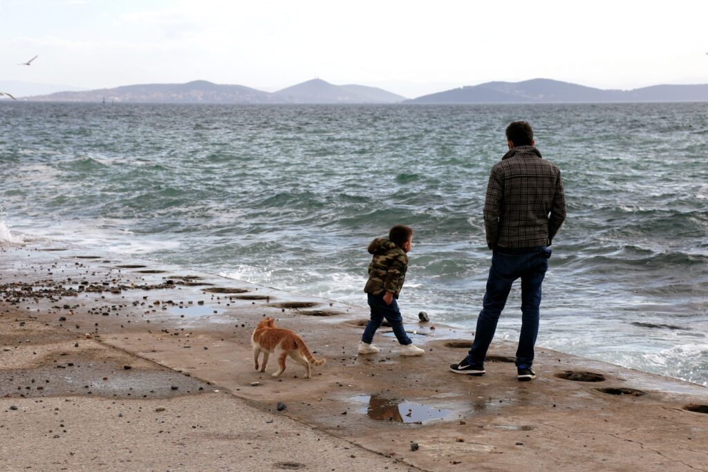 man in black and white plaid dress shirt standing beside girl in black jacket on beach